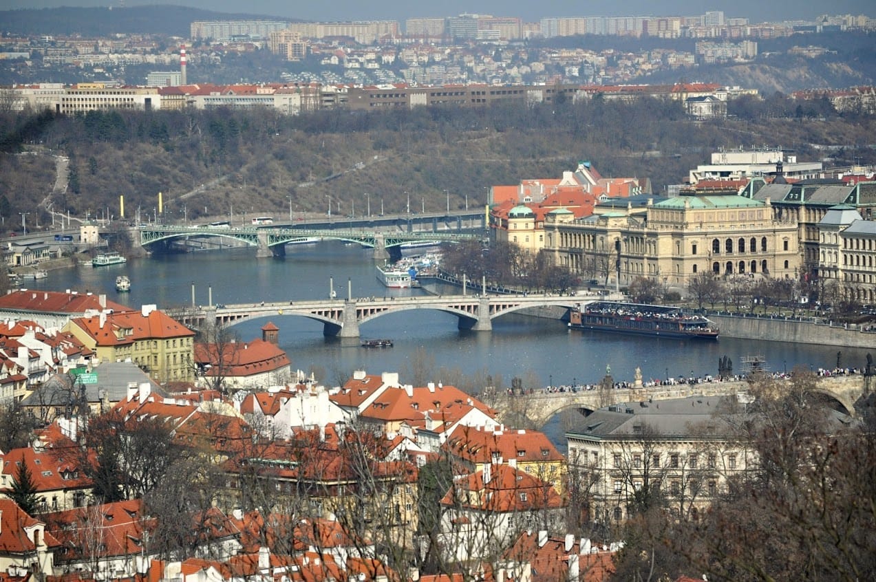 Pohled z výšky na Vltavu v Praze s Mánesovým a Čechovým mostem a Rudolfinem, v popředí červené střechy Malé Strany