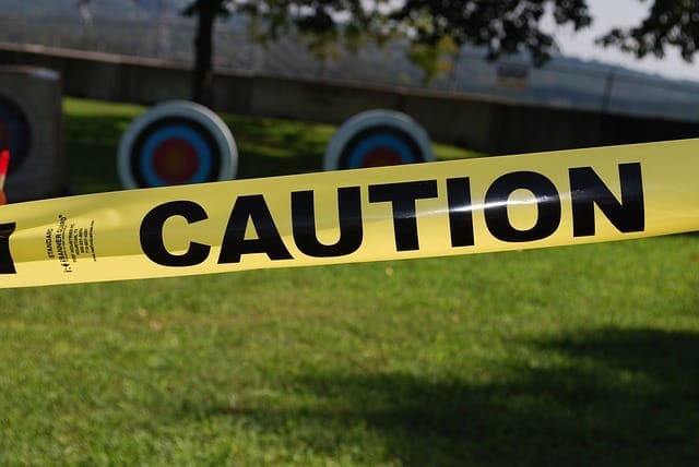 Žlutá výstražná páska s nápisem CAUTION natažená před terči pro lukostřelbu na trávníku