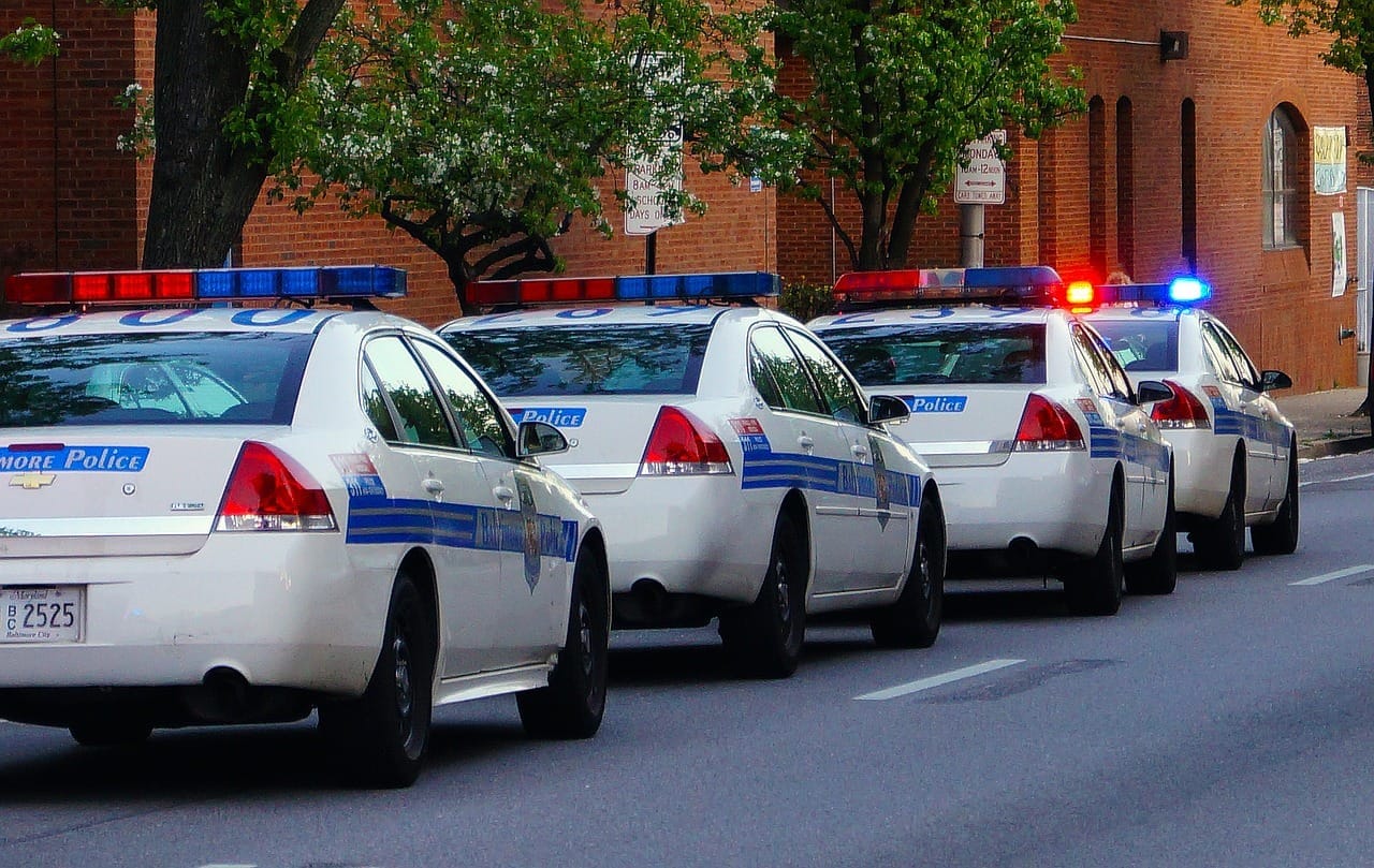 Čtyři policejní vozy Baltimore Police se zapnutými modrými a červenými světly stojí v řadě u obrubníku
