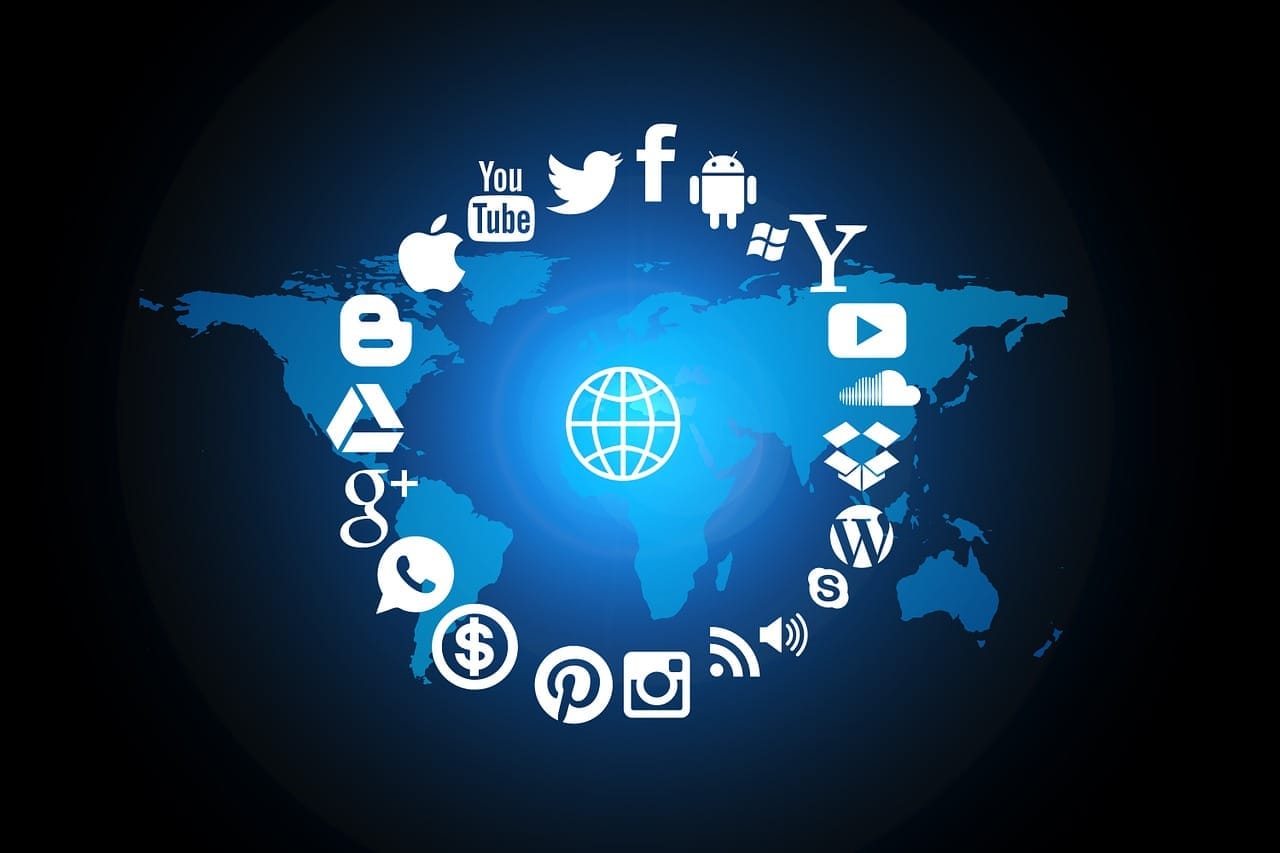 Modrá mapa světa s ikonami sociálních sítí a služeb — YouTube, Twitter, Facebook, Android, Apple, Google+, Pinterest, Instagram, Skype, WordPress — v kruhu kolem symbolu zeměkoule