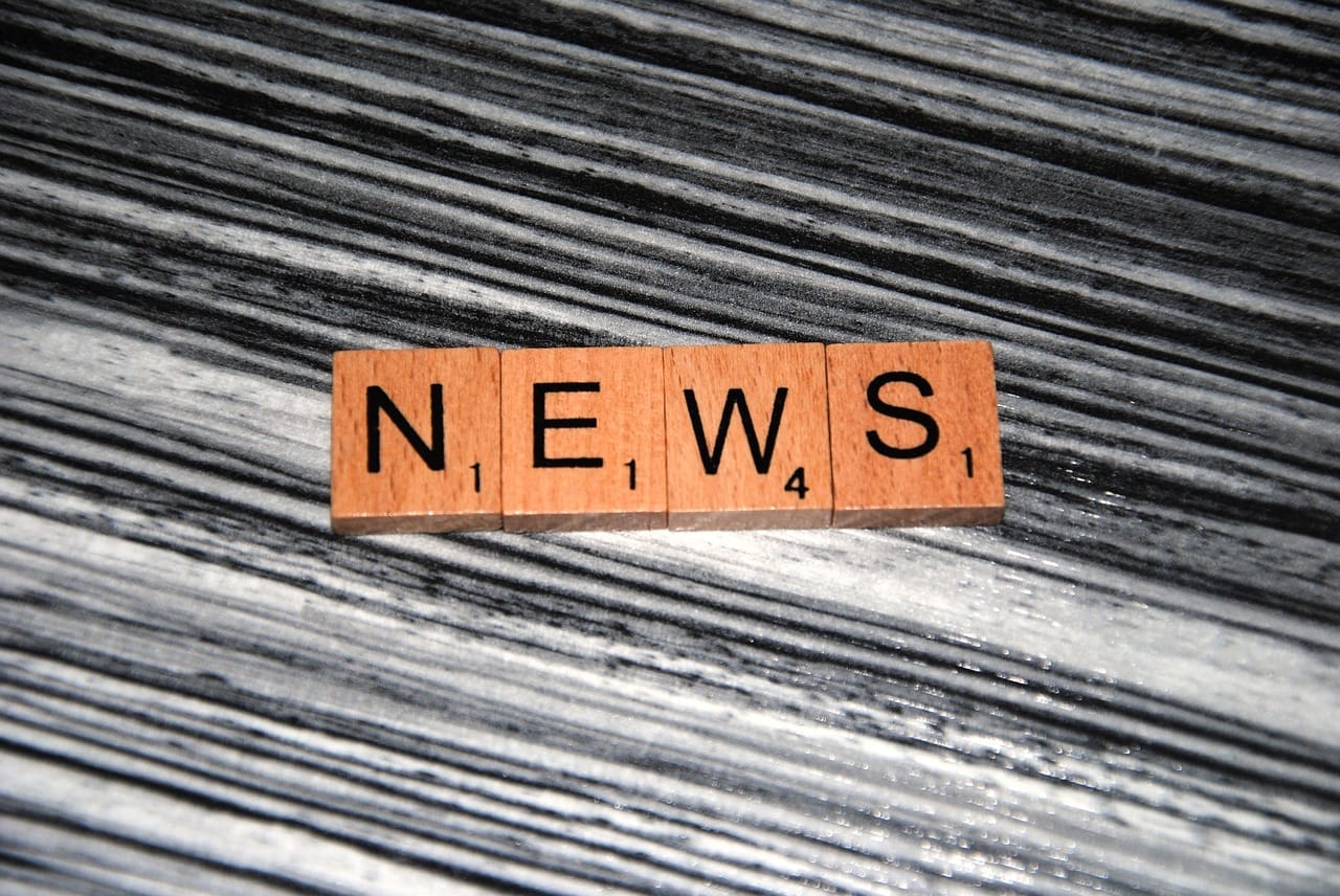 Dřevěné hrací kameny ze scrabble skládající slovo NEWS na pruhovaném dřevěném podkladu