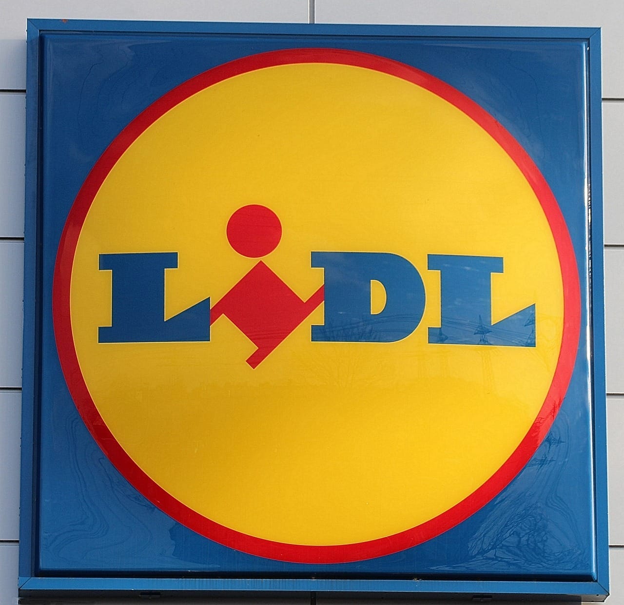 Logo obchodního řetězce Lidl na fasádě prodejny – žlutý kruh s červeným okrajem a modrým nápisem LIDL