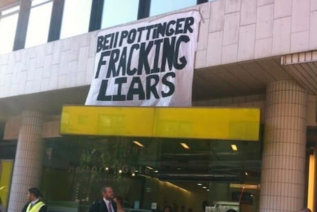 Bílý transparent s ručně psaným textem „Bell Pottinger fracking liars“ zavěšený nad vchodem do budovy, dole dva muži