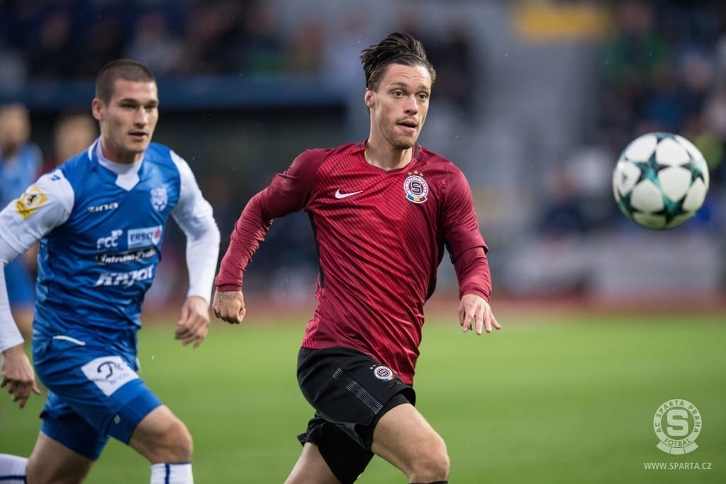 Fotbalista v bordovém dresu Sparty Praha běží za míčem, sleduje ho protihráč v modrobílém