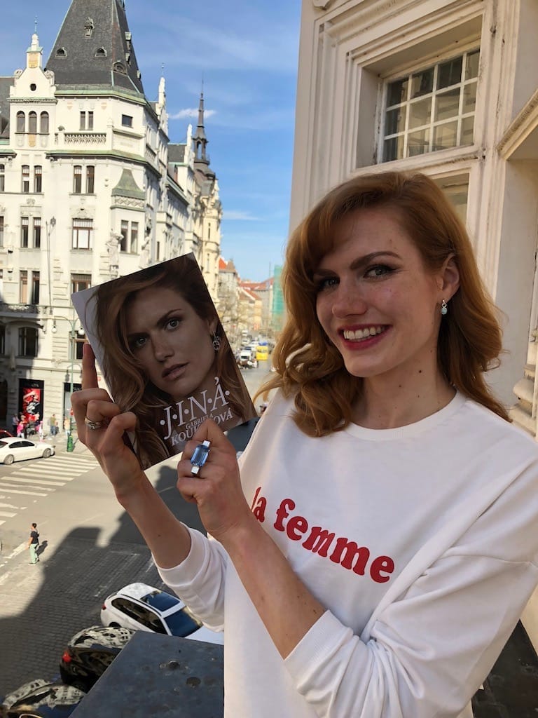 Gabriela Koukalová v bílé mikině s nápisem „la femme“ drží na balkoně svou knihu Jiná