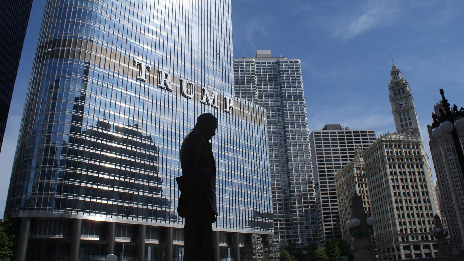 Silueta sochy muže před prosklenou budovou Trump Tower v Chicagu s velkým nápisem TRUMP
