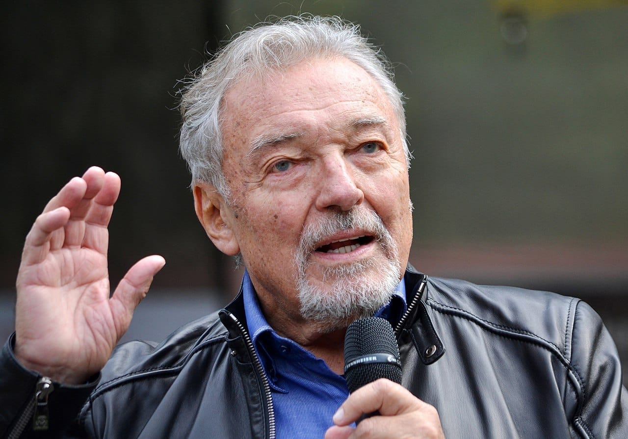 Karel Gott s mikrofonem v ruce a zvednutou paží mluví do publika