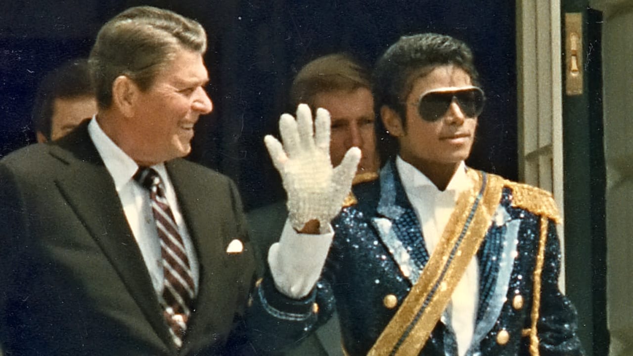 Ronald Reagan v obleku vedle Michaela Jacksona v tmavých brýlích, flitrové uniformě se zlatými šňůrami a bílé rukavici, kterou mává