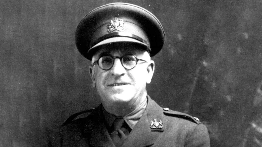 Černobílý portrét Franka Foleyho v důstojnické uniformě s čepicí a brýlemi s kulatými obroučkami