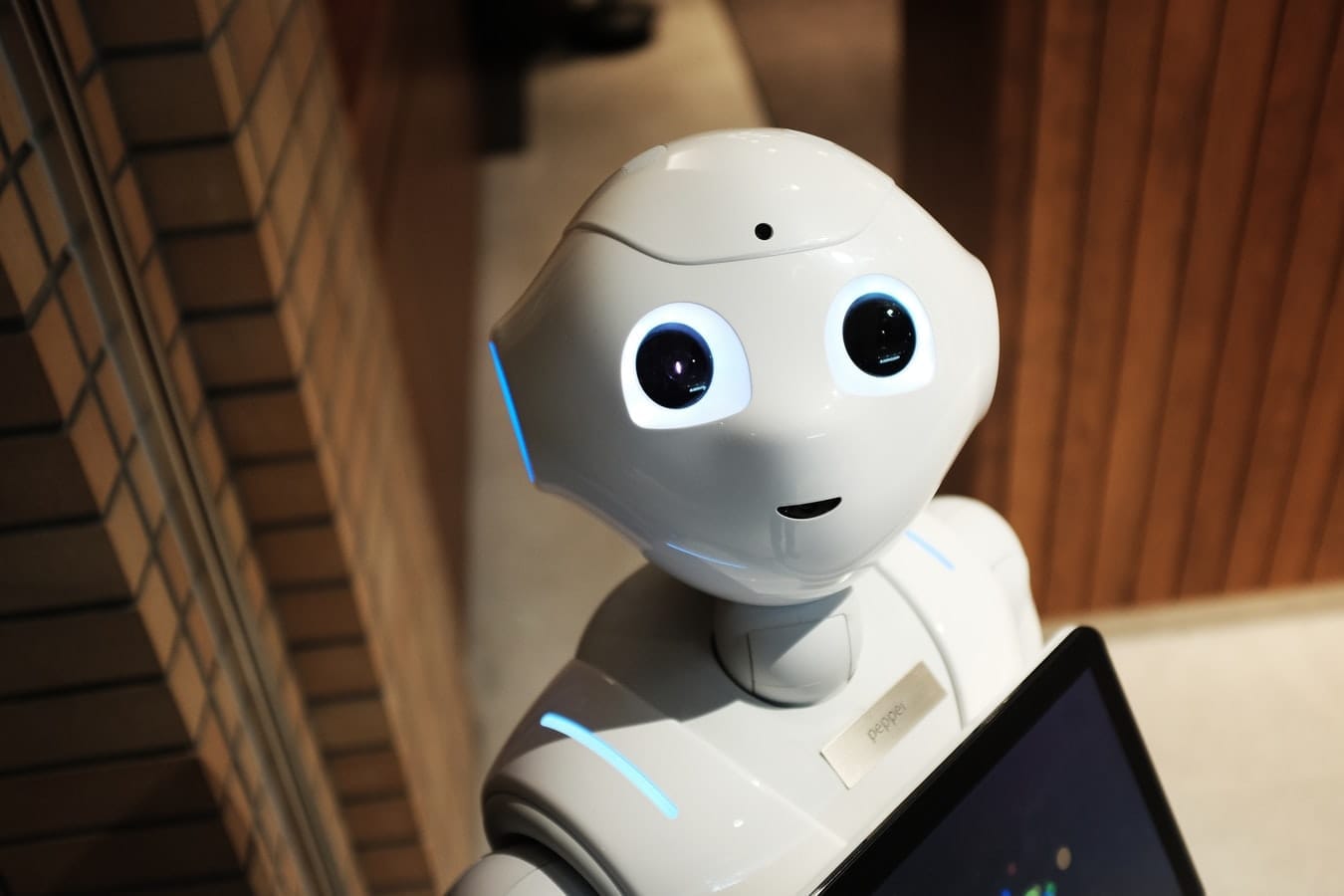 Bílý humanoidní robot Pepper s velkýma očima a displejem na hrudi