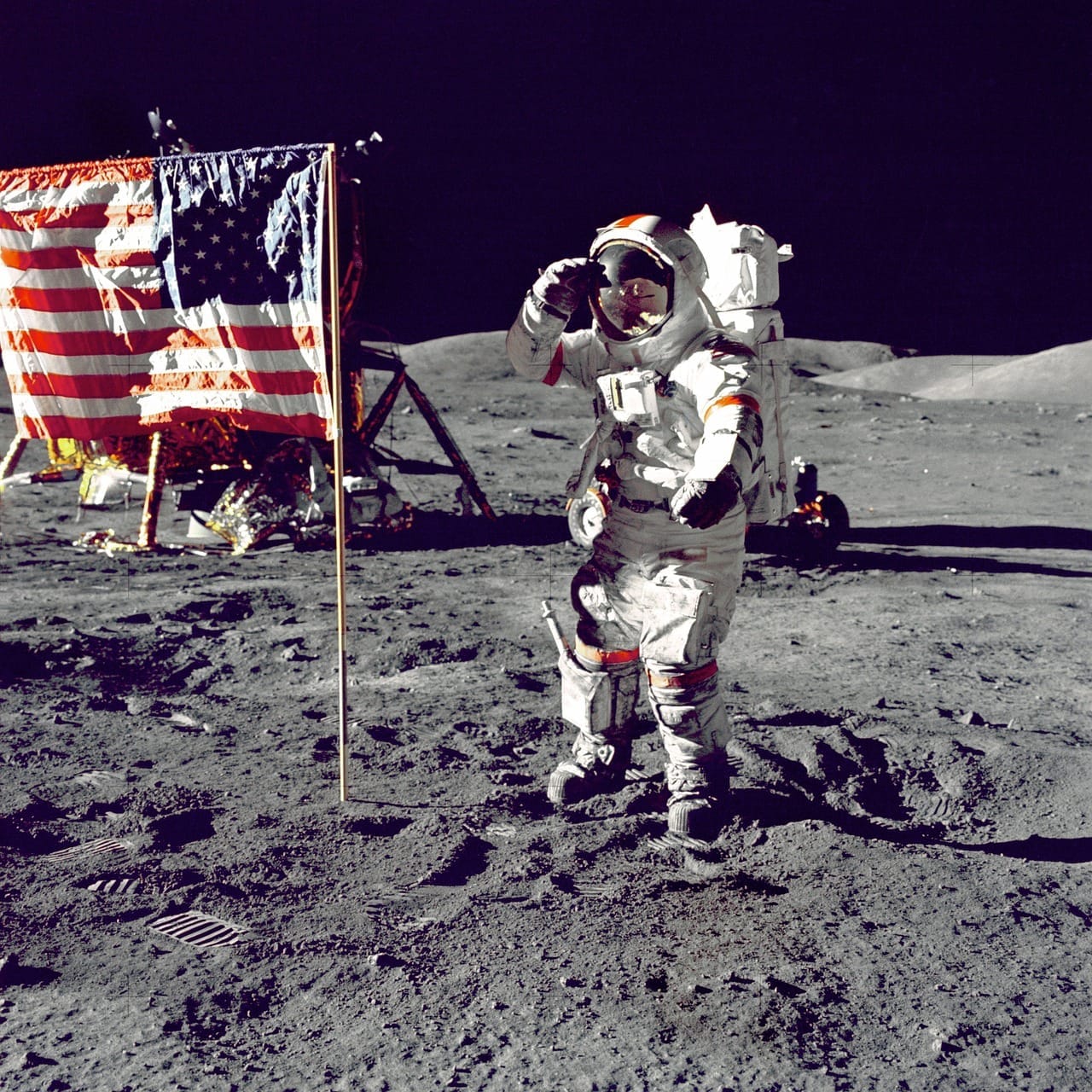 Salutující astronaut ve skafandru u americké vlajky na povrchu Měsíce, v pozadí lunární modul
