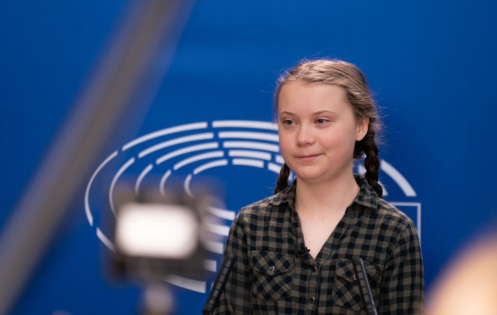 Greta Thunbergová v károvené košili před modrou stěnou s logem Evropského parlamentu