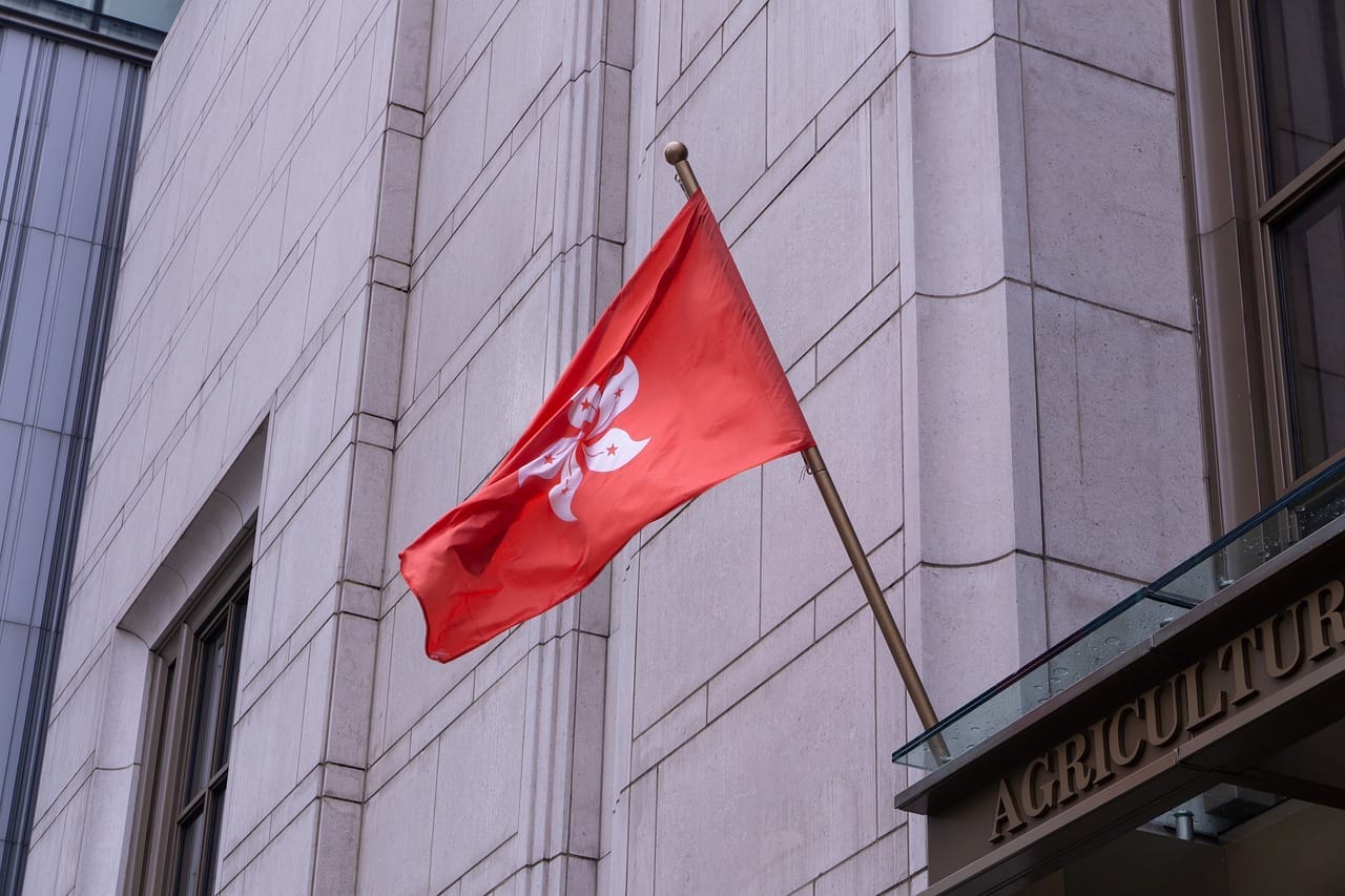 Červená vlajka Hongkongu s bílým květem baiuhinie na žerdi kamenné budovy s nápisem AGRICULTURE
