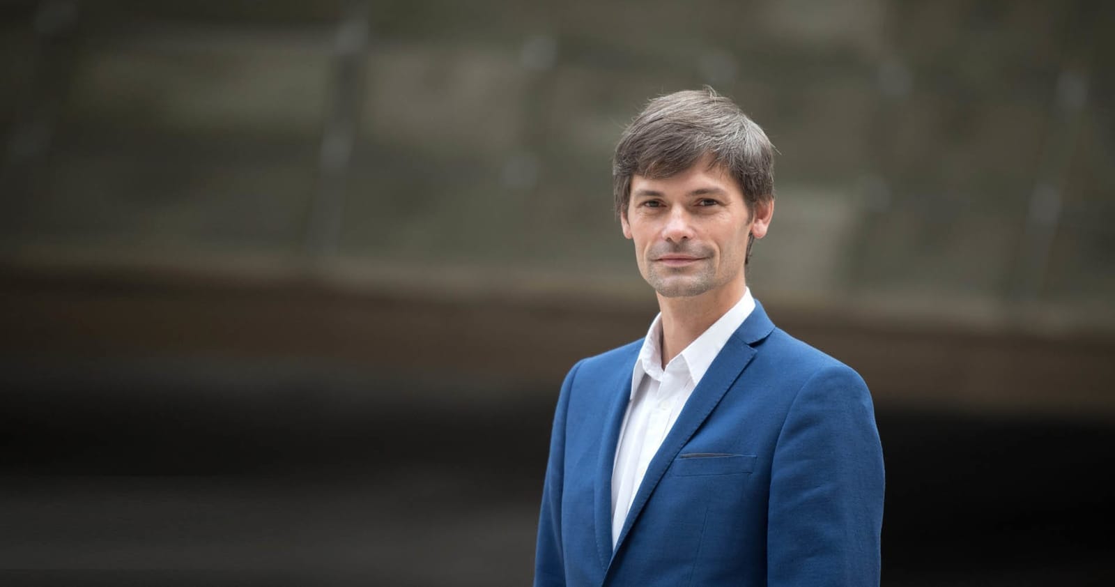 Senátor Marek Hilšer v modrém saku a bílé košili na portrétu před rozostřeným pozadím