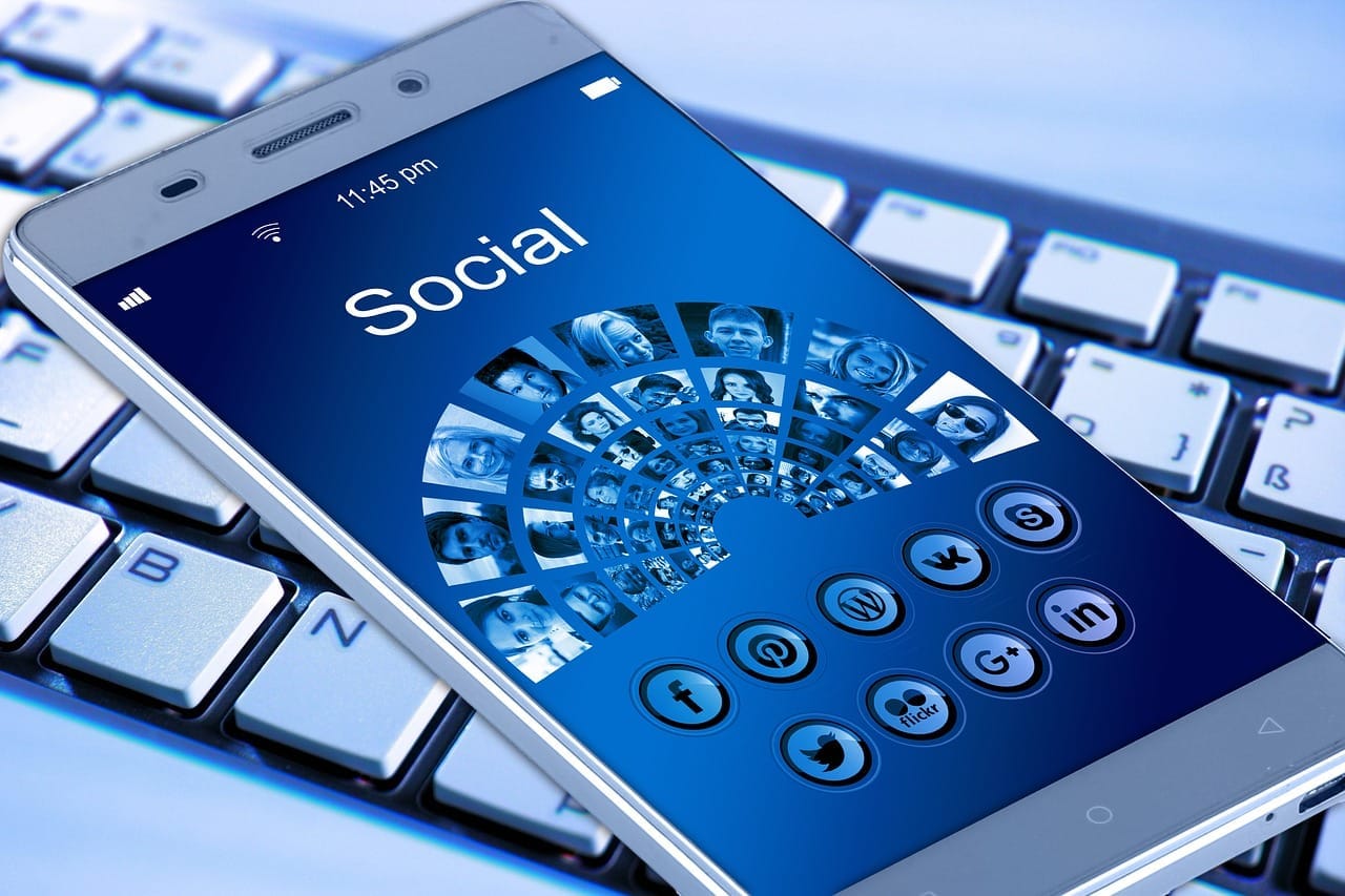 Mobilní telefon ležící na klávesnici s nápisem Social a ikonami sociálních sítí na displeji