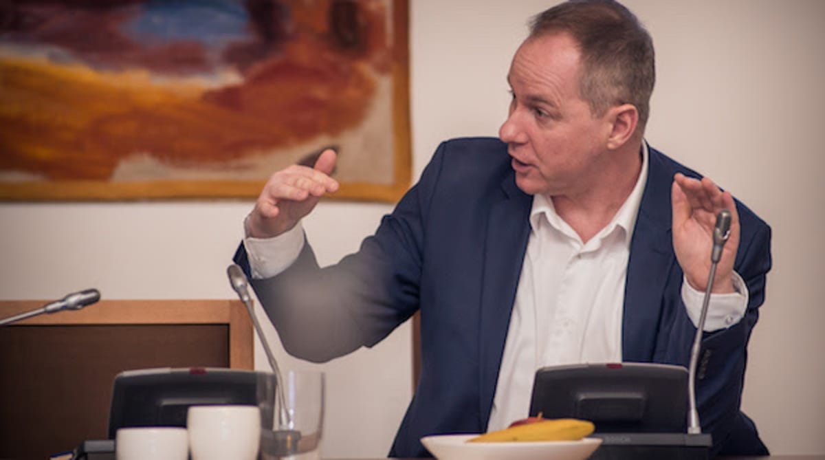 Petr Gazdík v tmavě modrém saku gestikuluje oběma rukama u mikrofonu při debatě
