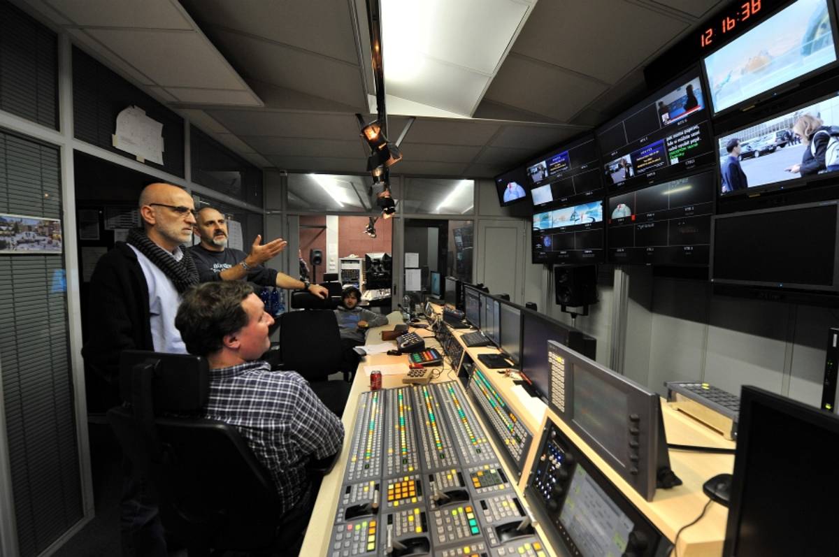 Televizní režie přenosového vozu s pultem, řadou monitorů a několika muži u ovládání