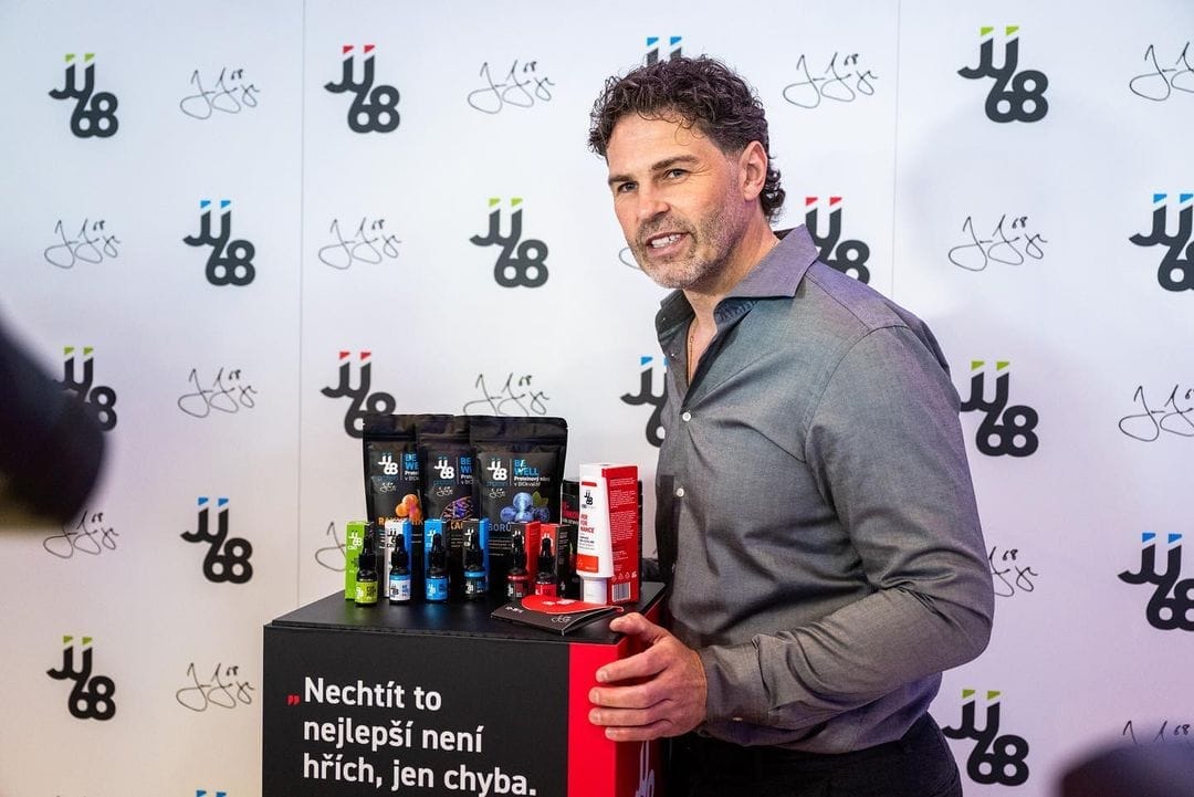 Jaromír Jágr u stojanu s produkty před stěnou s logy JJ68, na stojanu nápis „Nechtít to nejlepší není hřích, jen chyba.“