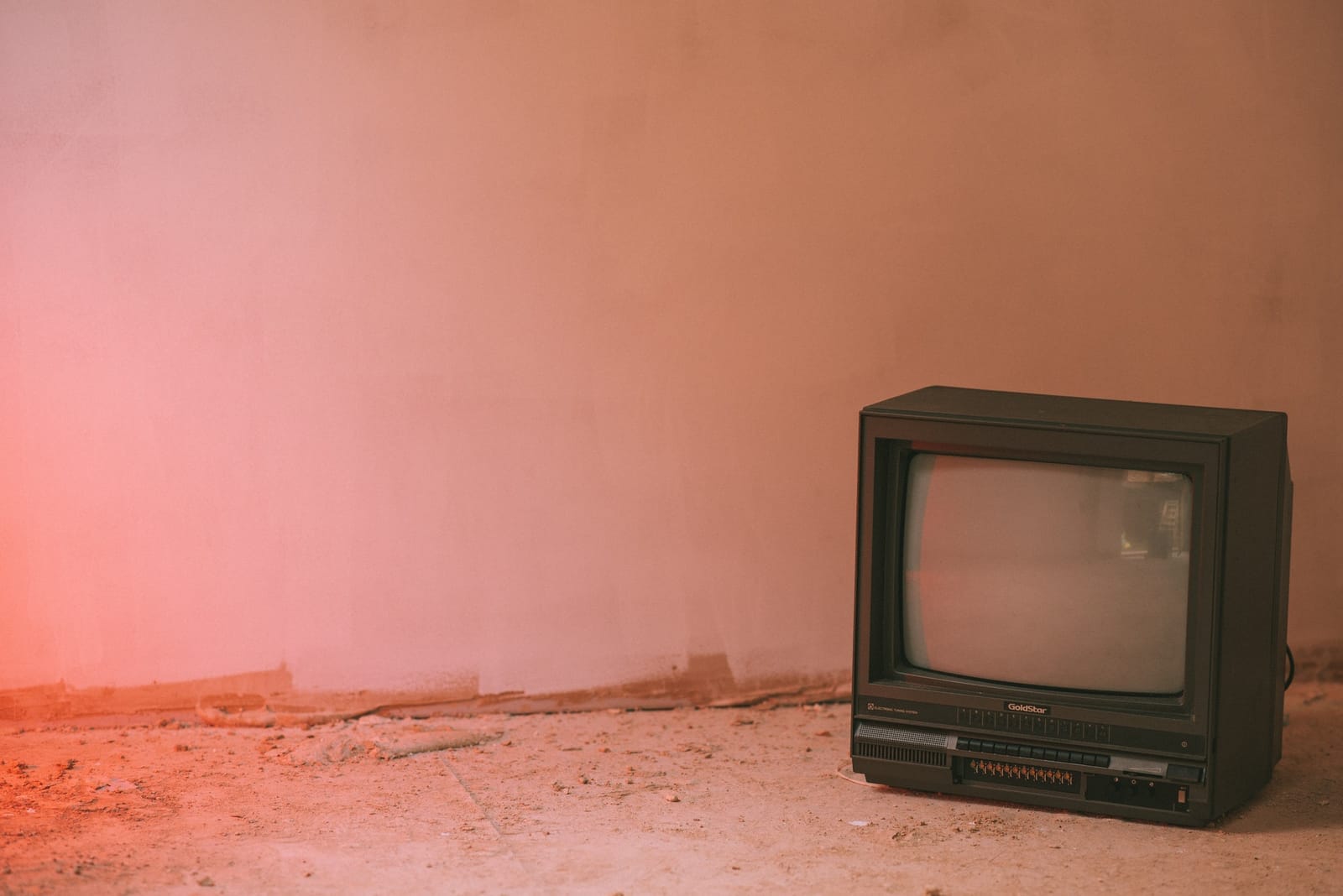 Starý televizor Goldstar stojící u zdi v prázdné zaprášené místnosti s růžovým nasvícením