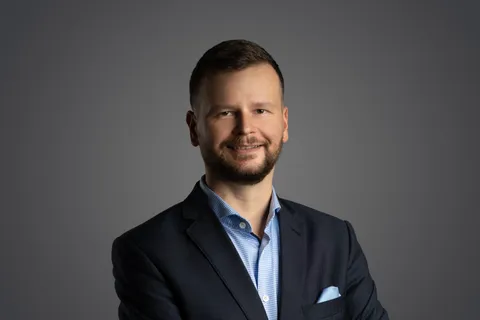 Filip Rožánek po ramena na tmavě šedém pozadí, s výrazným úsměvem